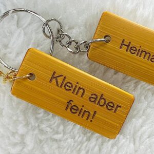 Rechteckige Schlüsselanhänger aus Bambus mit Lasergravur - Beispiele: 'Klein aber fein!' und 'Heimathafen' - mit Schlüsselringen in Gold- und Silberoptik und frei wählbarem Text oder Motiv