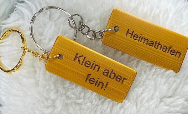 Rechteckige Schlüsselanhänger aus Bambus mit Lasergravur - Beispiele: 'Klein aber fein!' und 'Heimathafen' - mit Schlüsselringen in Gold- und Silberoptik und frei wählbarem Text oder Motiv